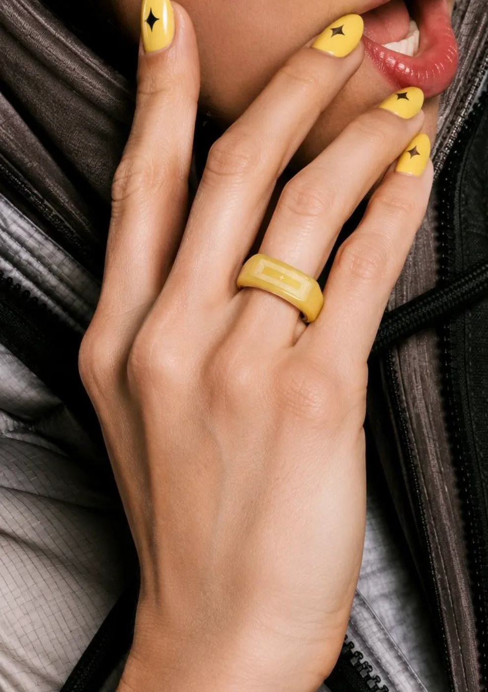 Close-up of a hand with yellow star nails and a yellow ring near lips
