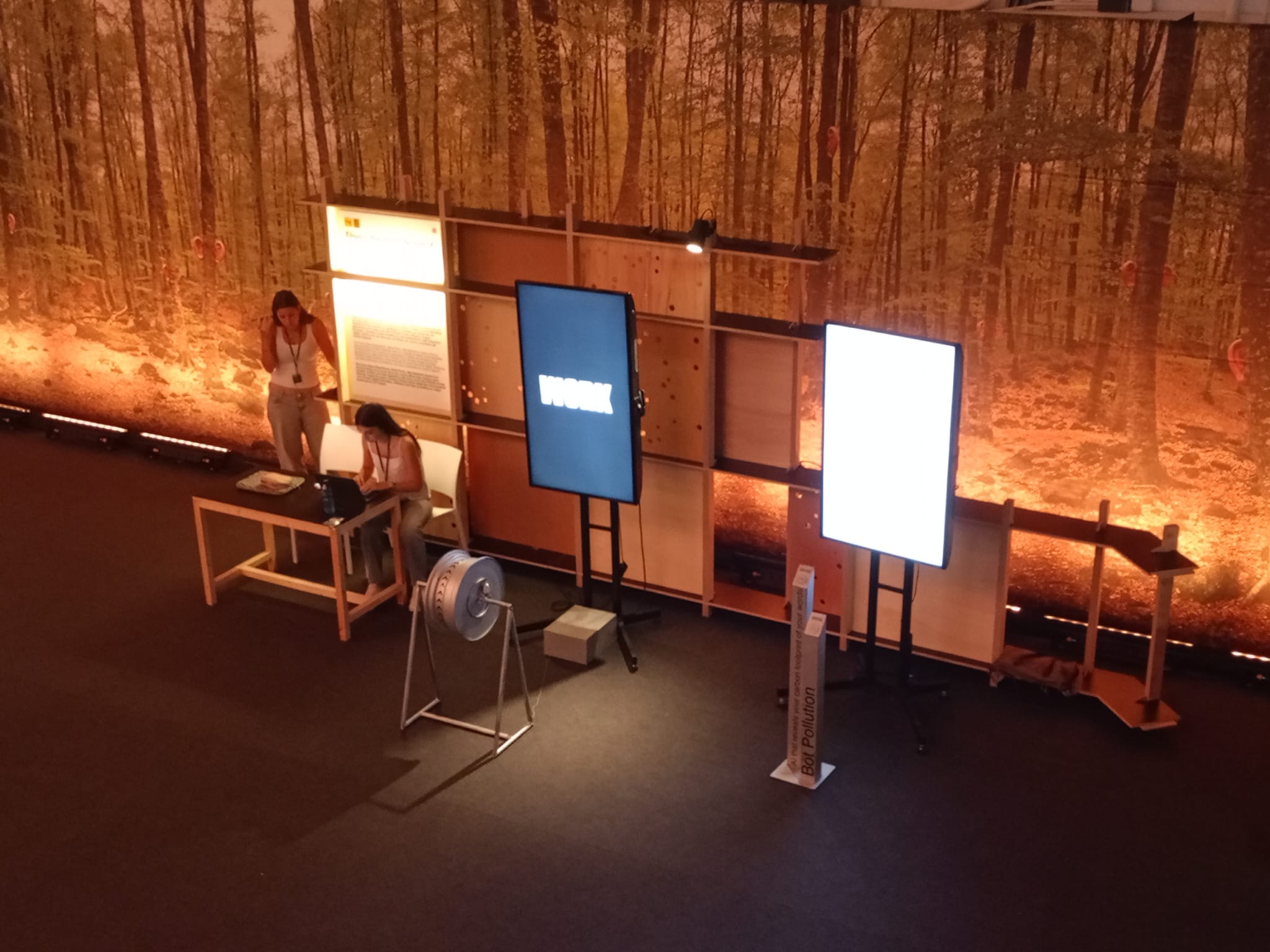 Aerial view of The Doom Race installation with two vertical screens and wheel on stand against a warm forest-fire backdrop