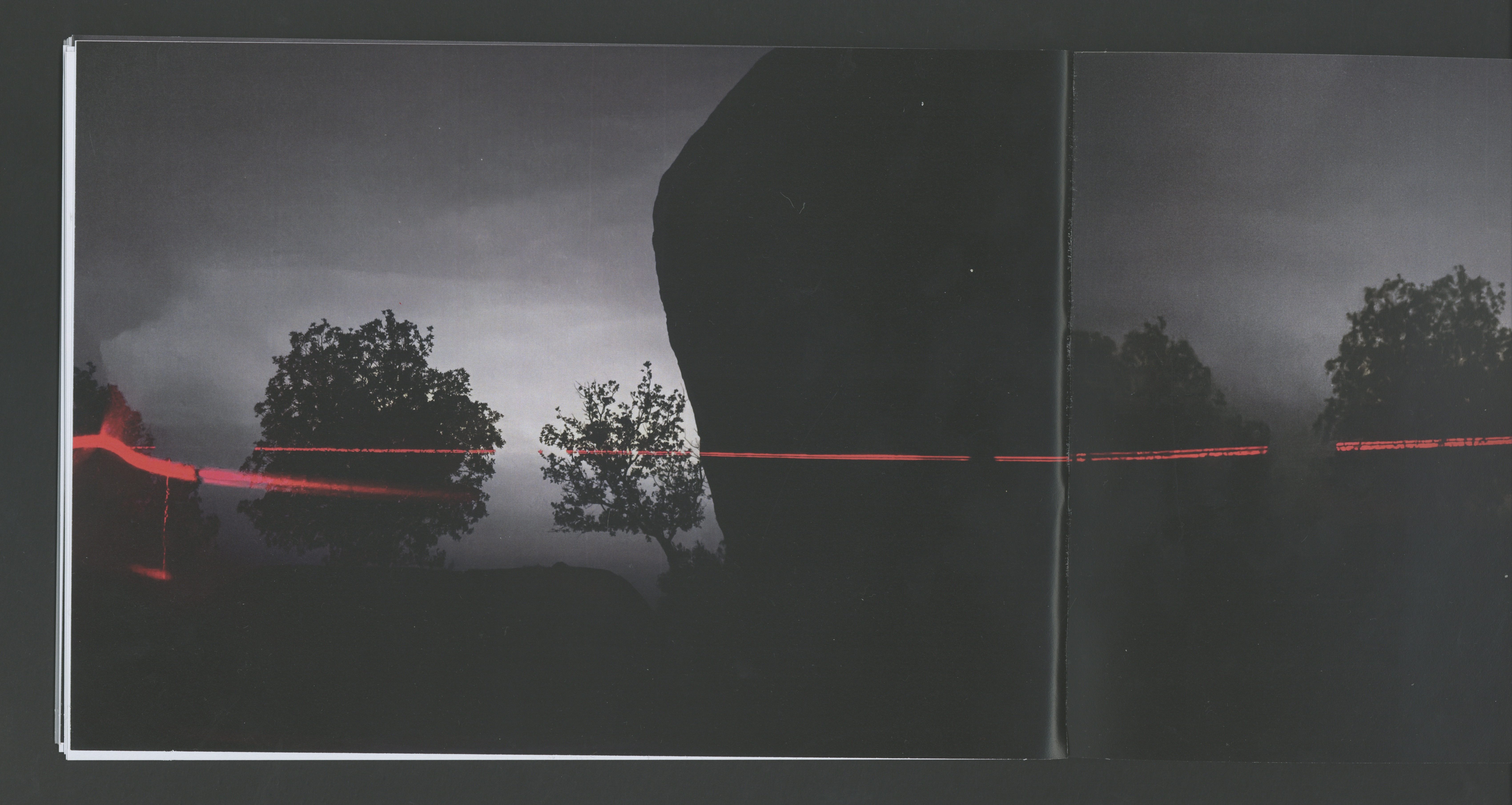 Book spread with red laser trail over dark landscape and silhouette of a large rock
