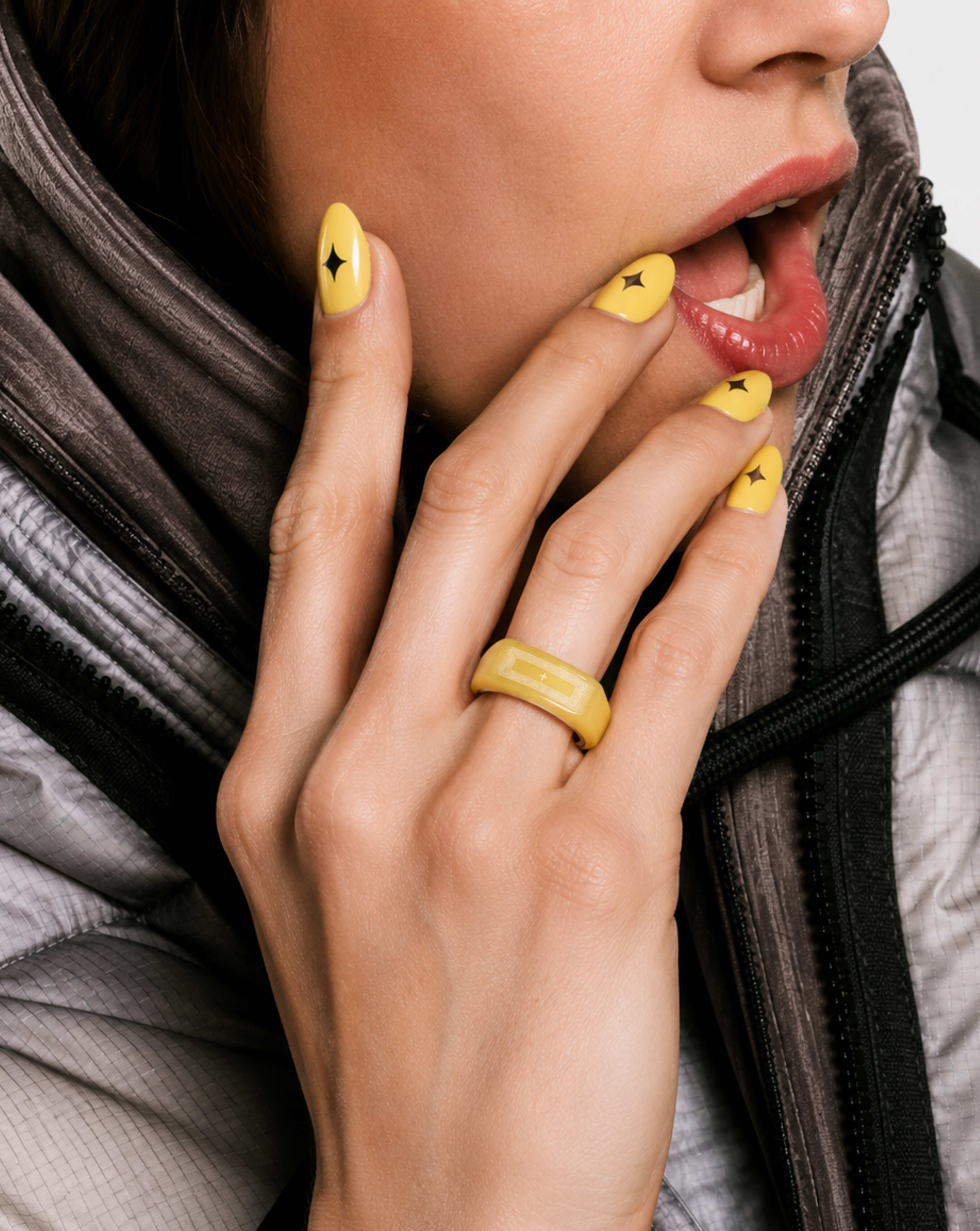 Close-up of a hand with yellow star nails and a yellow ring near lips