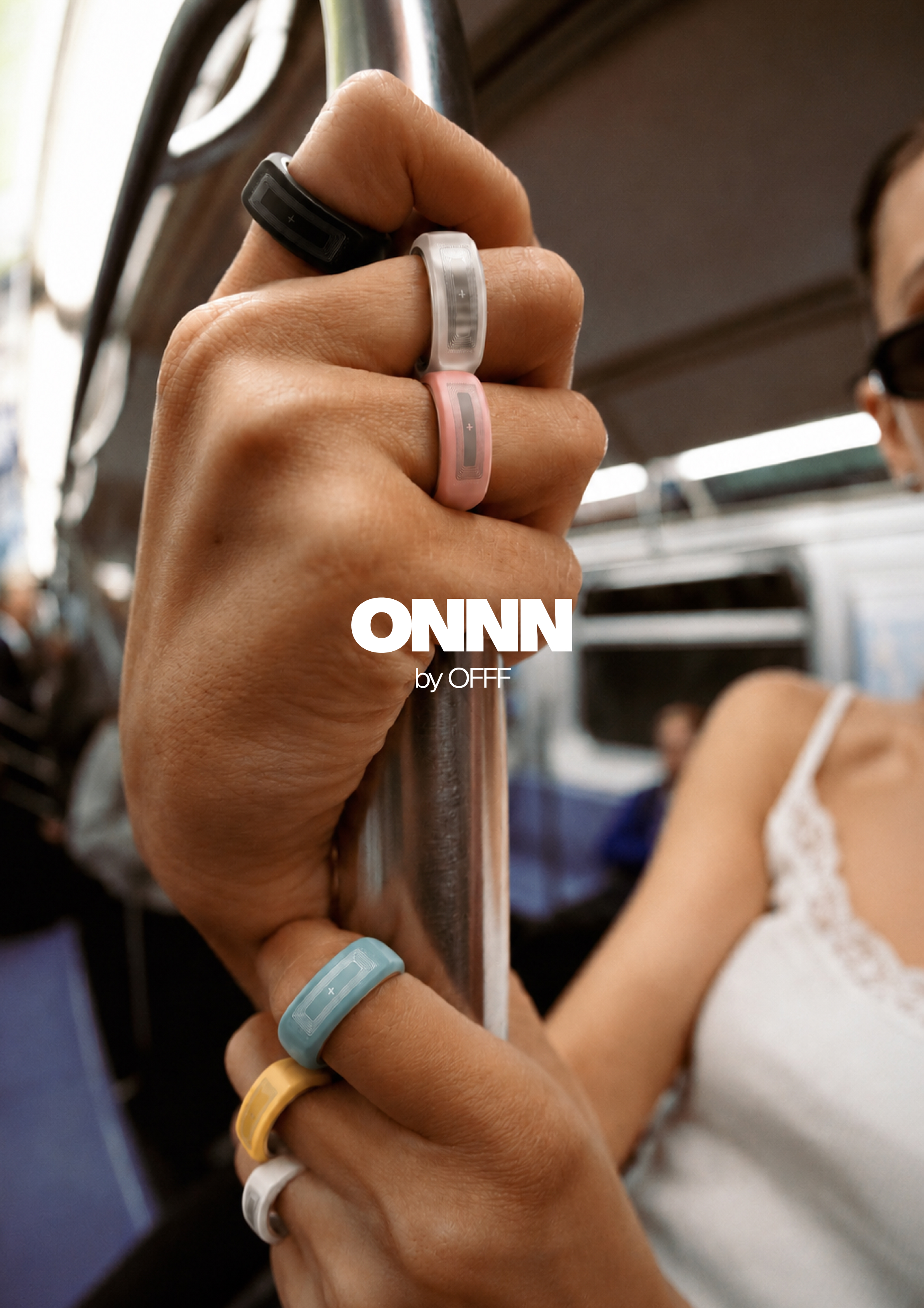 Hand gripping a subway bar wearing multiple coloured ONNN rings with ONNN by OFFF logo